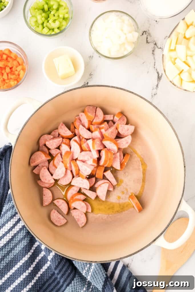 Sliced kielbasa sausage added to a large soup pot with oil, surrounded by bowls of chopped vegetables and potatoes.