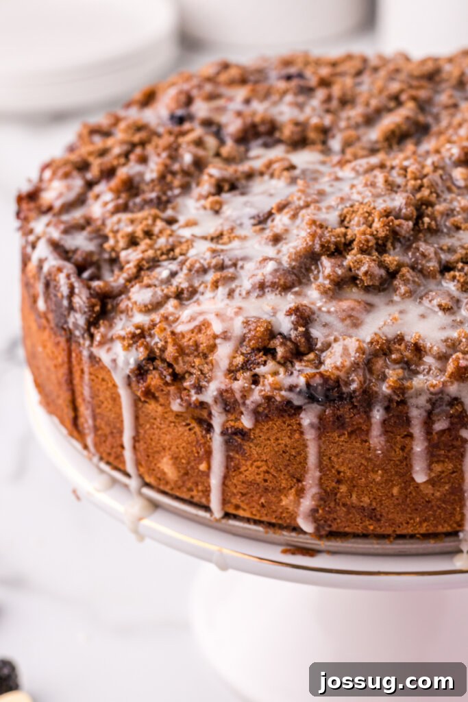 Whole blackberry lemon coffee cake on a white cake stand, drizzled with icing