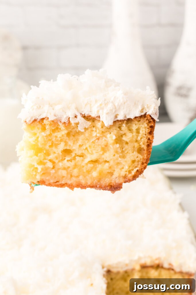 A large spatula lifting a perfect slice of Coconut Cream Poke Cake from a baking pan, showing its moist texture