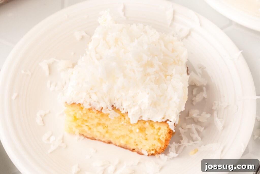 A close-up of a perfectly sliced Coconut Cream Poke Cake on a plate, highlighting its moist layers and creamy topping