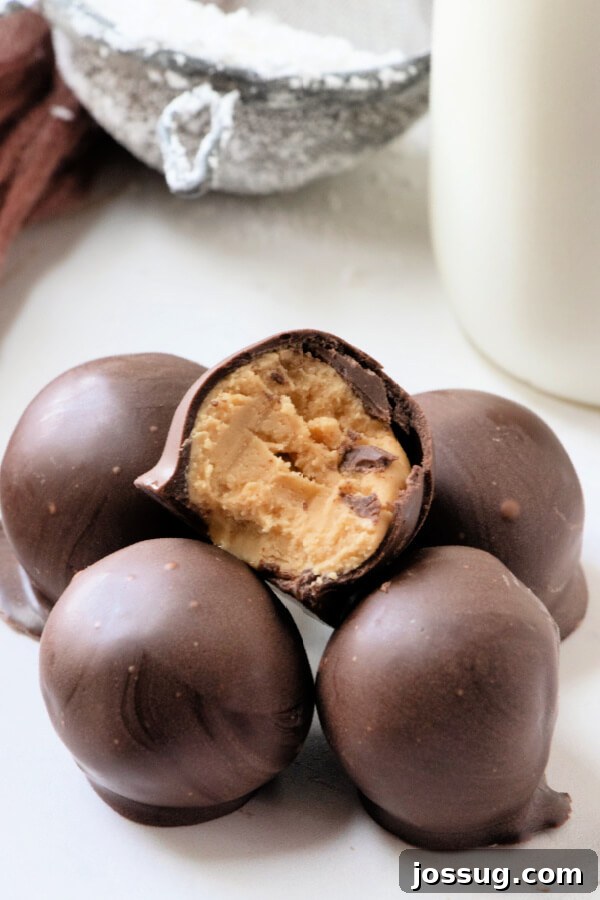 Decadent Peanut Butter Truffles 2 Peanut butter balls stacked on a board, one with a bite taken out, showcasing the creamy peanut butter filling and chocolate coating