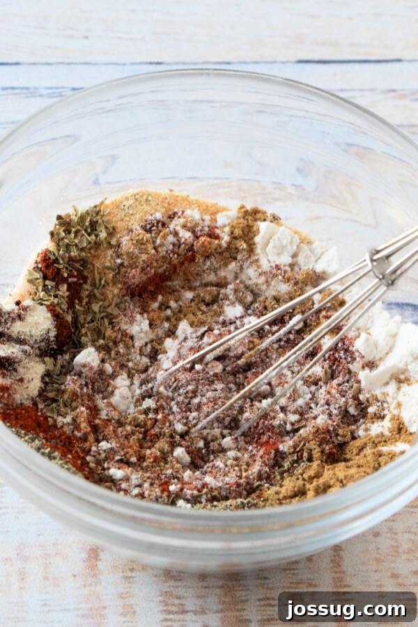 DIY Taco Spice Mix 4 Hands whisking together the spices in a clear glass bowl, blending them into a uniform homemade taco seasoning mix