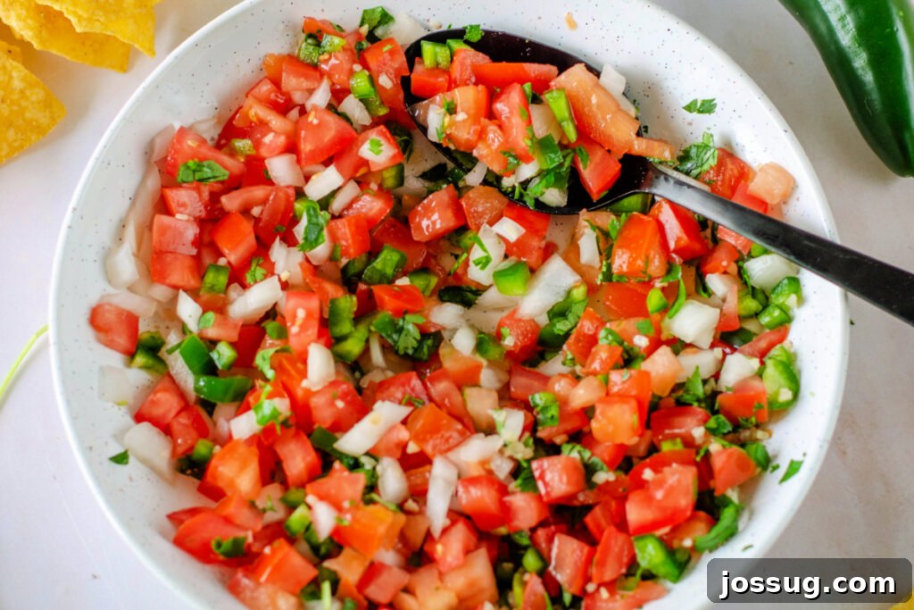 A close-up shot of freshly chopped tomatoes, peppers, onions, cilantro, and lime juice combined in a bowl, showcasing the vibrant colors of Pico de Gallo ingredients.