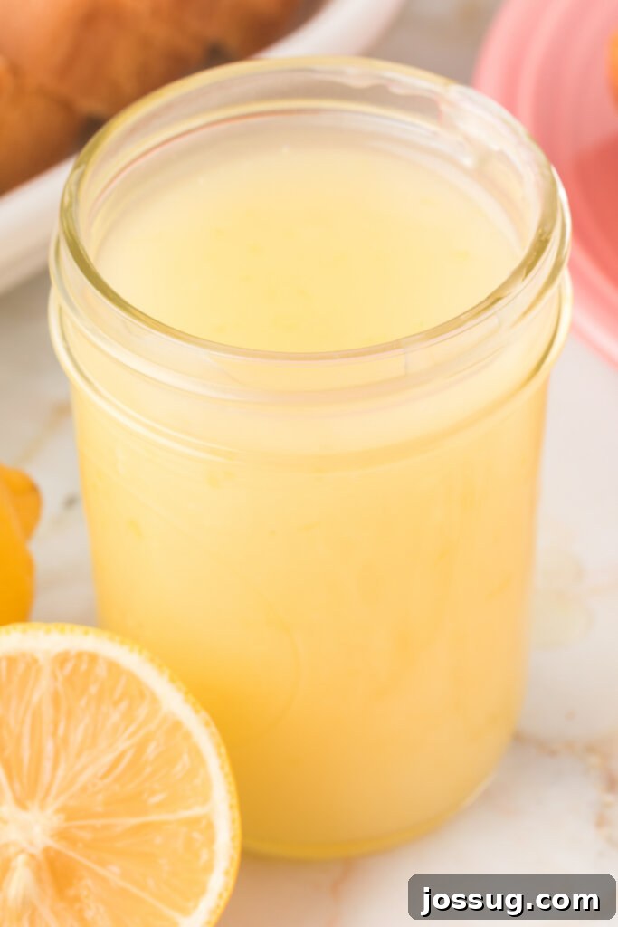 Closeup of bright yellow lemon sauce in a clear glass jar, ready to be served over desserts.