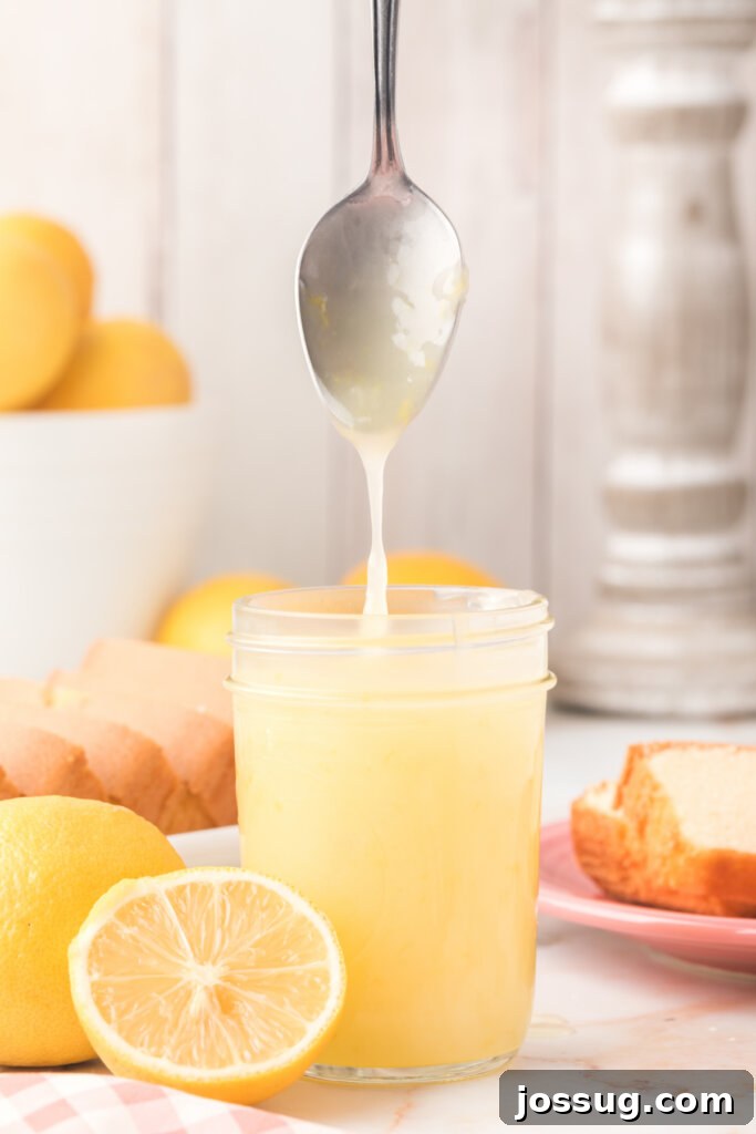Smooth, glossy lemon sauce drips from a spoon back into a glass jar, highlighting its perfect consistency.