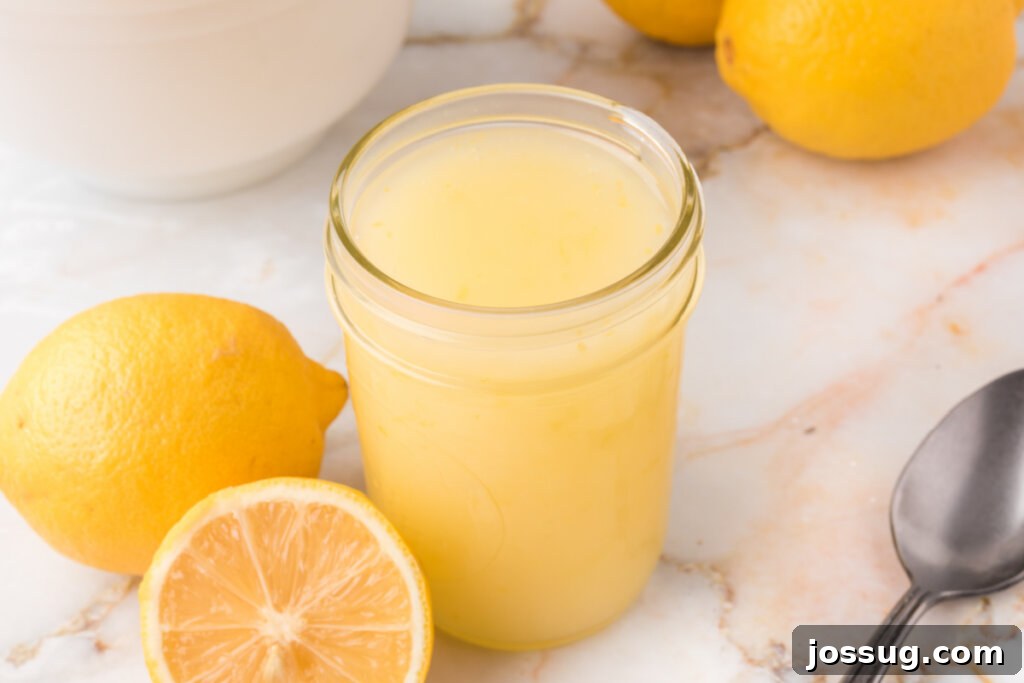 A jar of homemade lemon sauce surrounded by fresh whole and sliced lemons on a rustic surface.