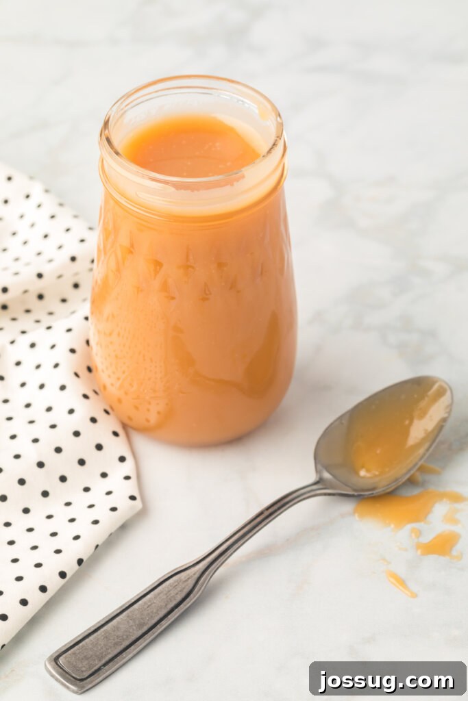 Decadent Caramel 3 Caramel sauce in a glass jar with a small spoon, ready to be served or stored.