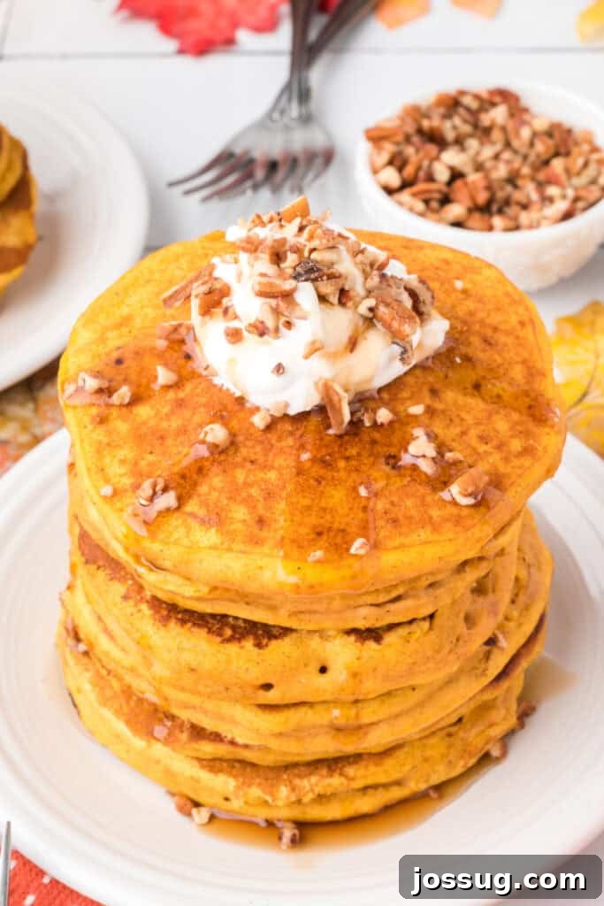 Close-up of fluffy pumpkin pancakes stacked high with whipped cream, pecans, and syrup drizzled on top