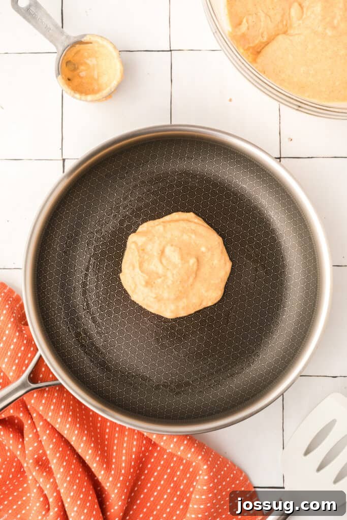 Pumpkin pancake cooking in frying pan with ladle and batter bowl in the background