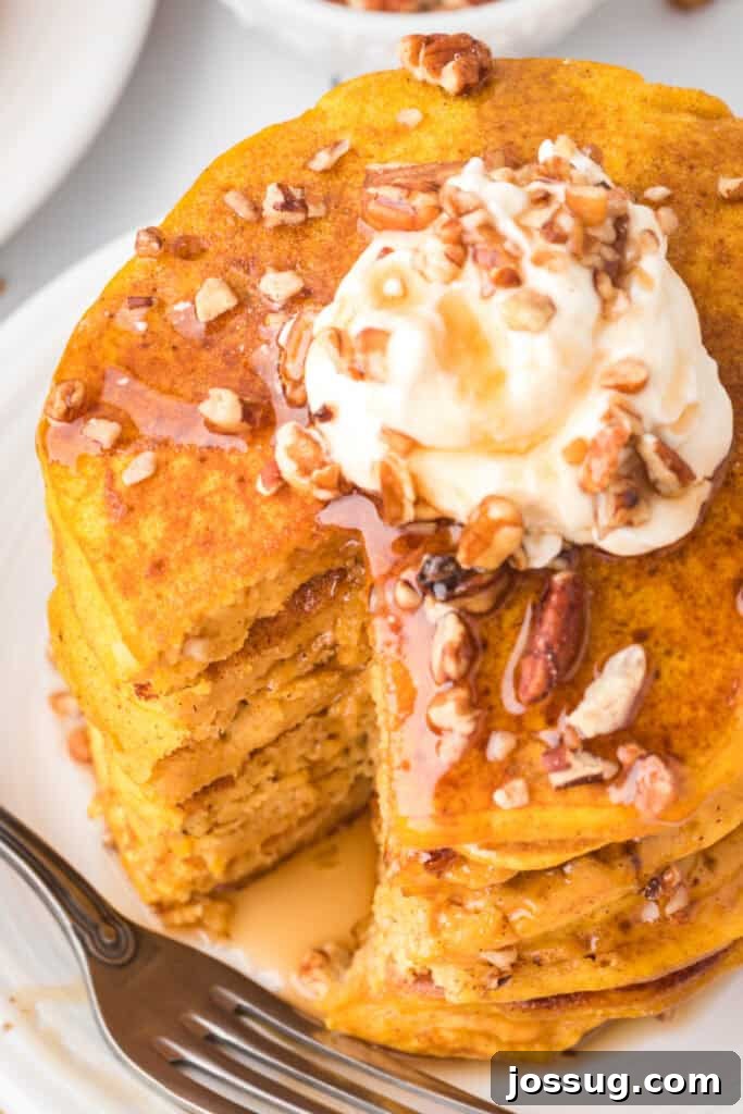 Stack of pumpkin pancakes with syrup and whipped cream, showing a cut section revealing soft, fluffy texture