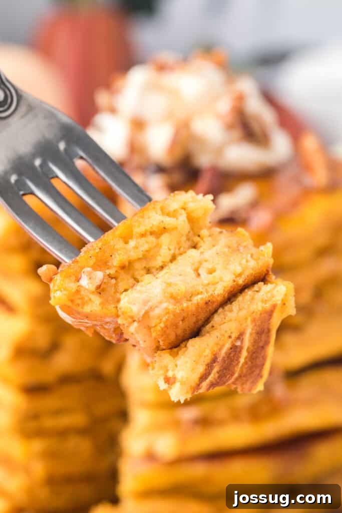 Fork holding a bite of pumpkin pancakes with syrup and pecans, blurred background of stacked pancakes