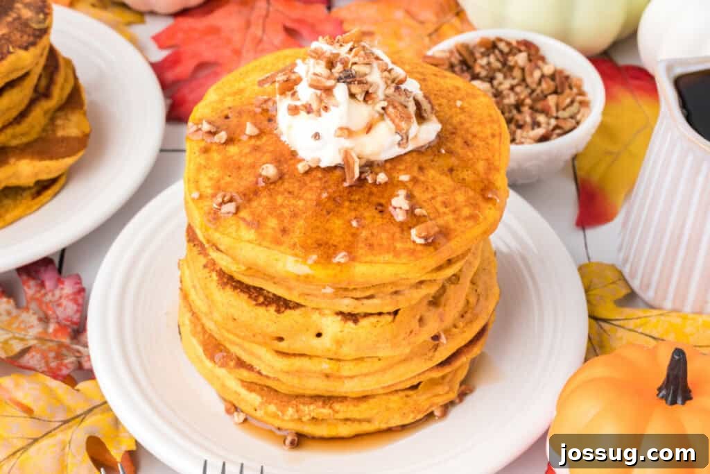 Overhead view of pumpkin pancakes on a white plate topped with whipped cream and pecans, surrounded by fall leaves