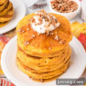 Square crop of pumpkin pancakes topped with whipped cream, chopped pecans, and syrup for a cozy fall breakfast scene