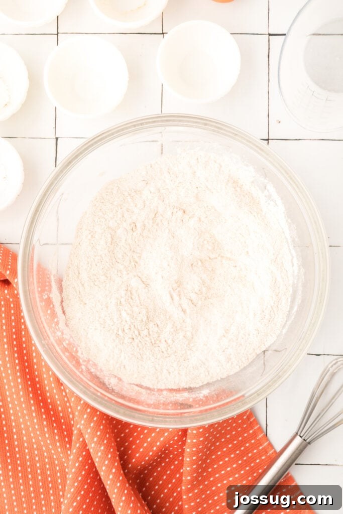 Bowl of combined dry ingredients for pumpkin pancakes with whisk and orange towel beside it