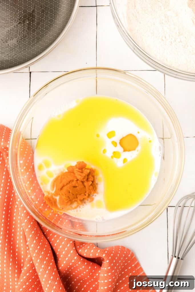 Wet ingredients including pumpkin purée, milk, oil, and egg in a glass bowl ready to be mixed