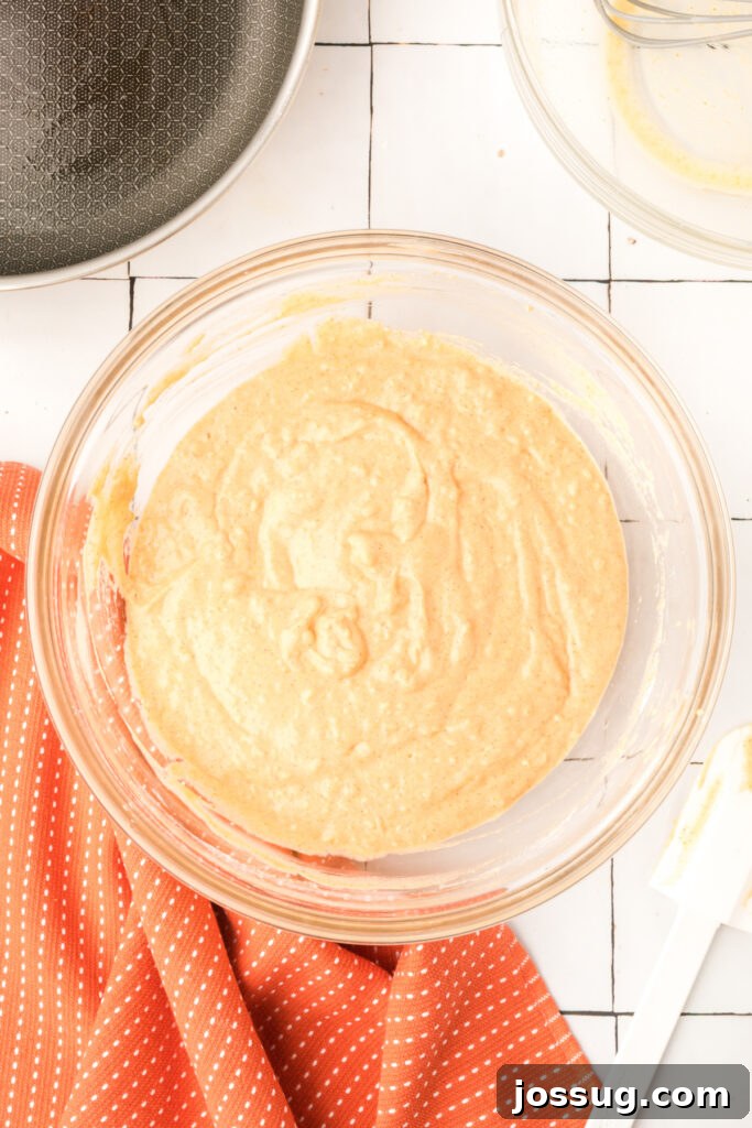 Smooth pumpkin pancake batter in a glass mixing bowl with spatula on the side