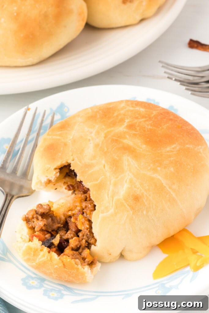 Loaded BBQ Bacon Cheeseburger Buns 2 A delicious BBQ Bacon Cheeseburger Bun with a bite removed, showcasing the savory filling inside, served on a white plate.