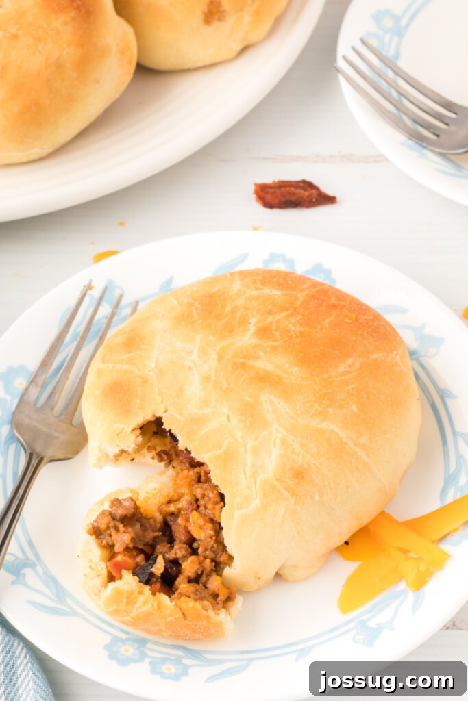 Loaded BBQ Bacon Cheeseburger Buns 4 A whole BBQ Bacon Cheeseburger Bun placed on a white plate with a fork, ready to be enjoyed.