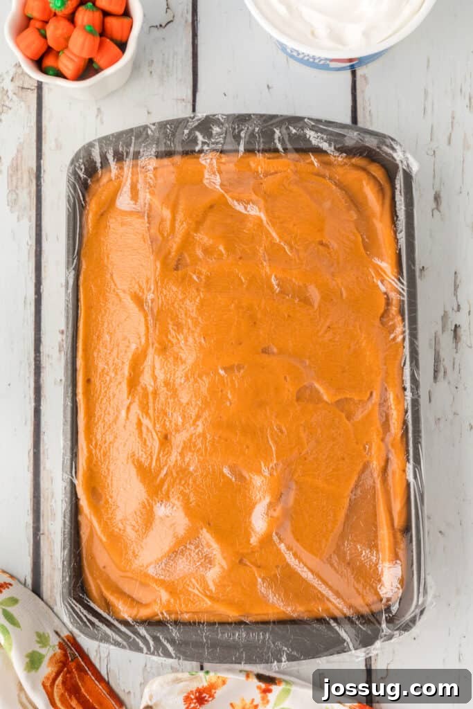 Decadent Pumpkin Spice Poke Cake 12 Plastic wrap covering the chilled pumpkin pudding cake in the pan