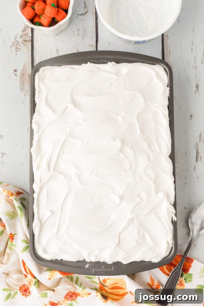 Decadent Pumpkin Spice Poke Cake 13 Overhead shot of cake topped with a thick layer of whipped topping in a pan