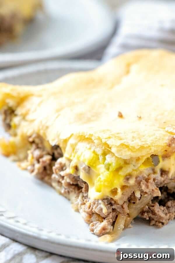 A delectable piece of White Castle Casserole on a white plate, close up, showing layers of beef, cheese, and golden-brown crescent roll.