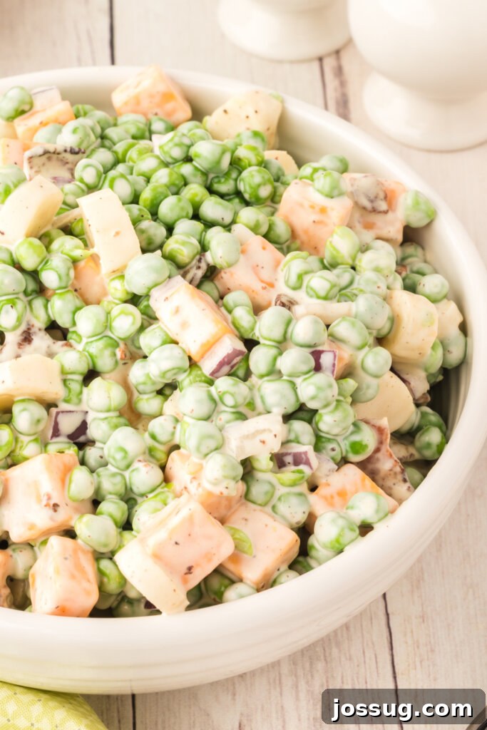 Velvety Pea Salad 2 A beautifully presented bowl of creamy pea salad with visible bacon bits, cheese cubes, and red onion, garnished and ready to serve.