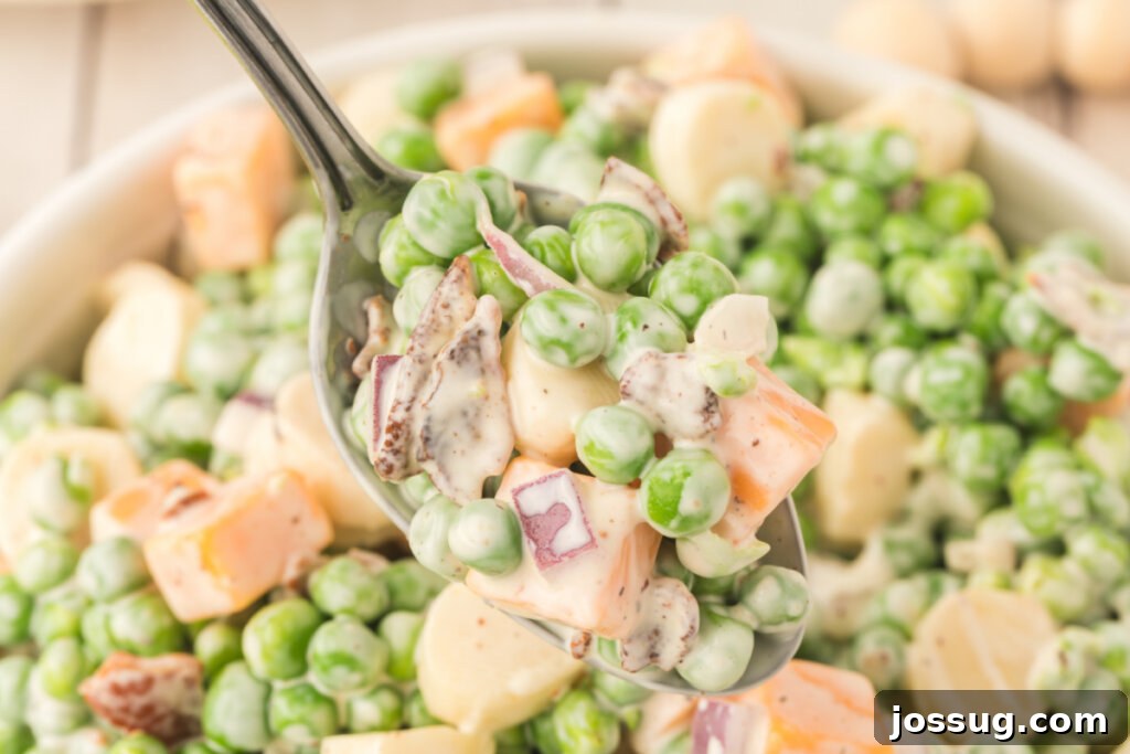 Velvety Pea Salad 5 A close-up photograph of a small portion of creamy pea salad on a spoon, highlighting its rich texture and appealing ingredients like cheese and bacon.