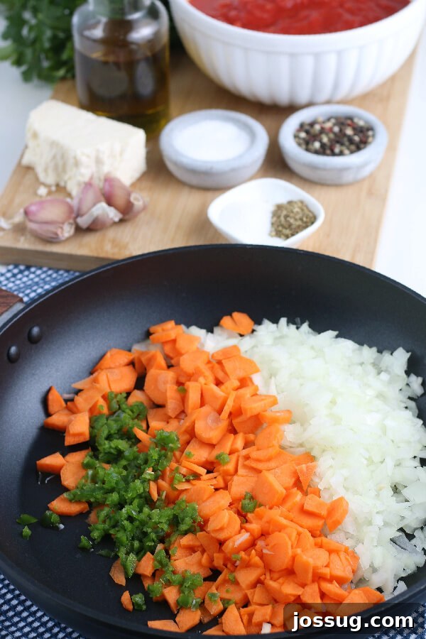 Freshly chopped vegetables, including carrots, onions, and jalapeño, sautéing in a pan with olive oil