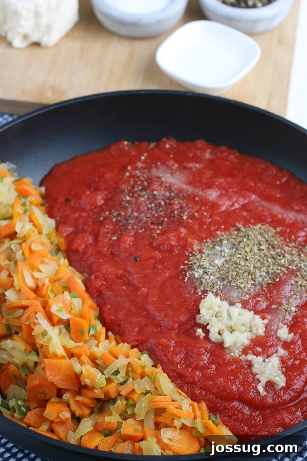 The rich tomato and herb sauce simmering in a pan, infused with garlic, oregano, and other aromatics