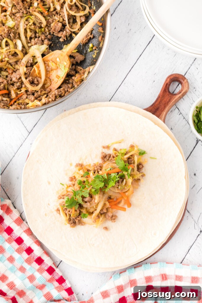 A large flour tortilla laid flat, with a generous scoop of the savory Thai pork and coleslaw filling placed in the center, ready to be rolled.