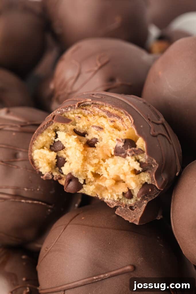 Pile of chocolate chip cookie dough truffles with one cut open to reveal soft cookie dough filling, garnished with a sprinkle of sea salt.