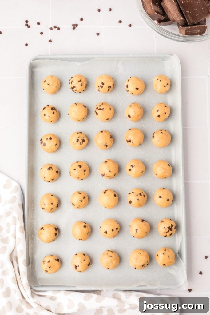 Perfectly rolled chocolate chip cookie dough balls, neatly arranged on a wax paper-lined baking sheet, awaiting their chocolate coating.