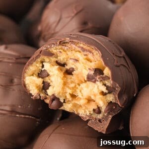 Square close-up of a bitten chocolate truffle with a soft, edible cookie dough filling and visible mini chocolate chips inside, illustrating its delicious texture.
