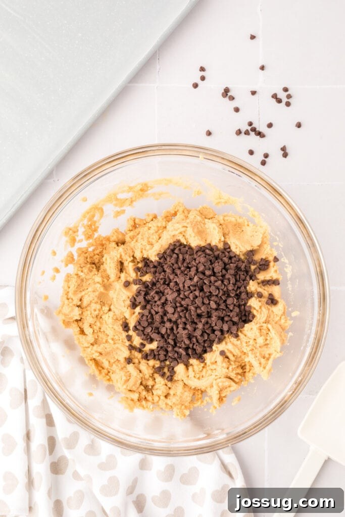 Mini chocolate chips carefully added to the prepared cookie dough mixture in a glass bowl, ready to be gently folded in.