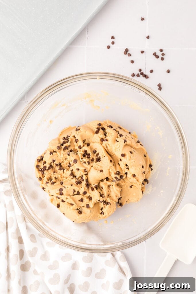 Cookie dough completely mixed with miniature chocolate chips, filling a large glass mixing bowl, showcasing its uniform texture and chip distribution.