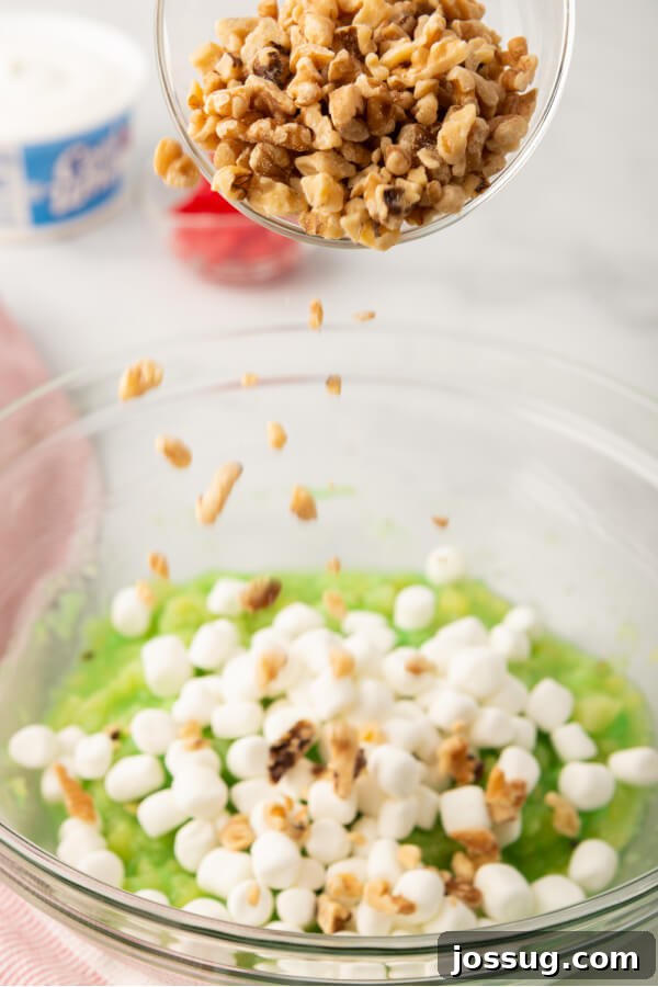 Green Jewel Salad 4 Miniature marshmallows and chopped nuts being carefully added to the pineapple-pudding mixture in a large mixing bowl.