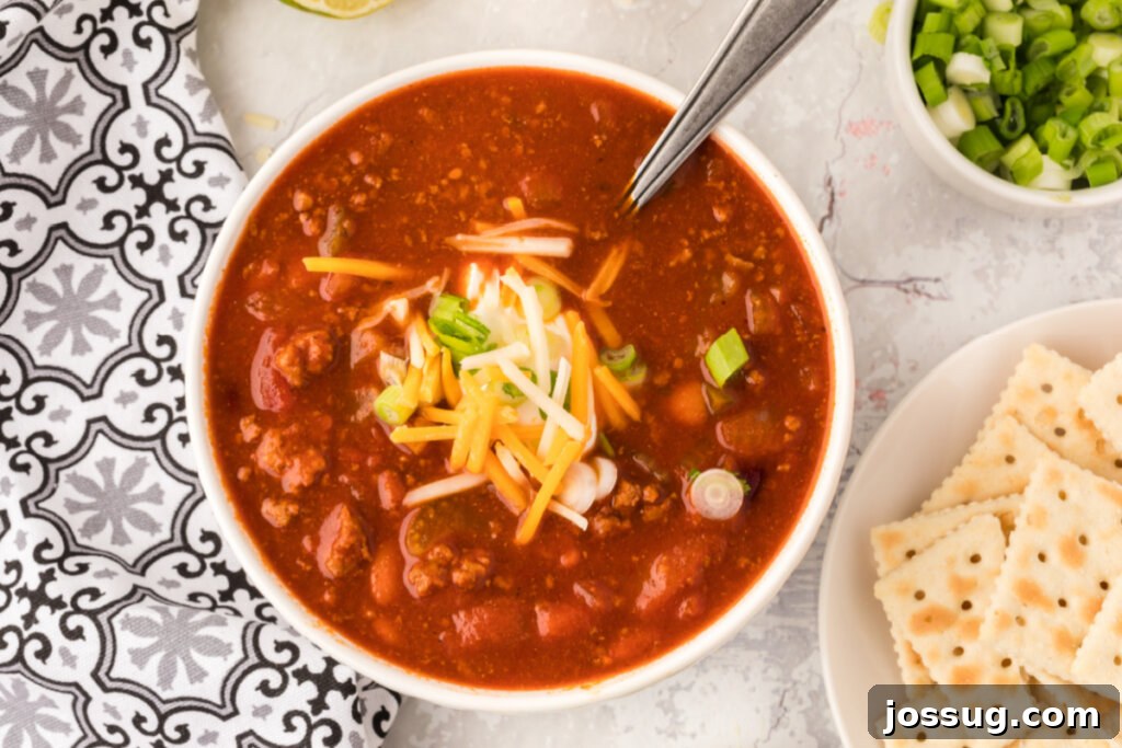A top-down view of a generously portioned bowl of Wendy's Copycat Chili, adorned with a generous layer of melted shredded cheddar cheese and vibrant green onions.