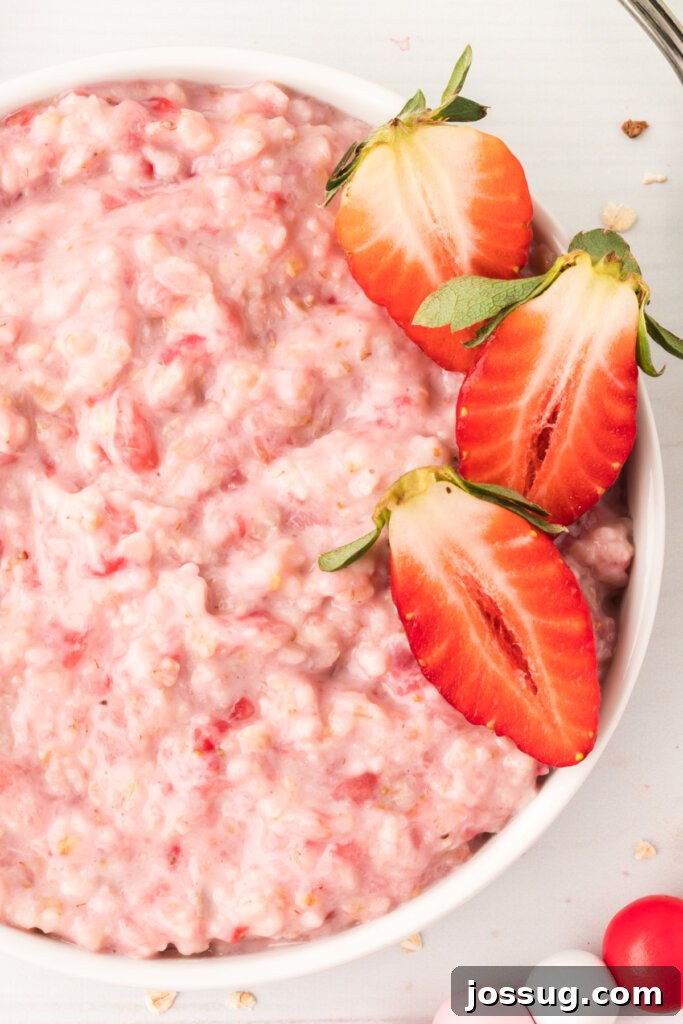 Strawberry Cloud Oatmeal 2 Closeup of a steaming bowl of homemade strawberries and cream oatmeal, garnished with fresh sliced strawberries and a drizzle of cream.