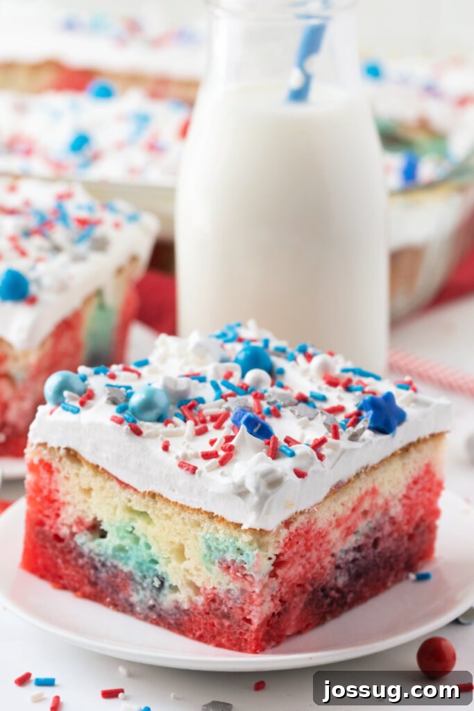 A vibrant slice of Patriotic Jello Poke Cake, showcasing its distinct red, white, and blue layers, served on a white plate