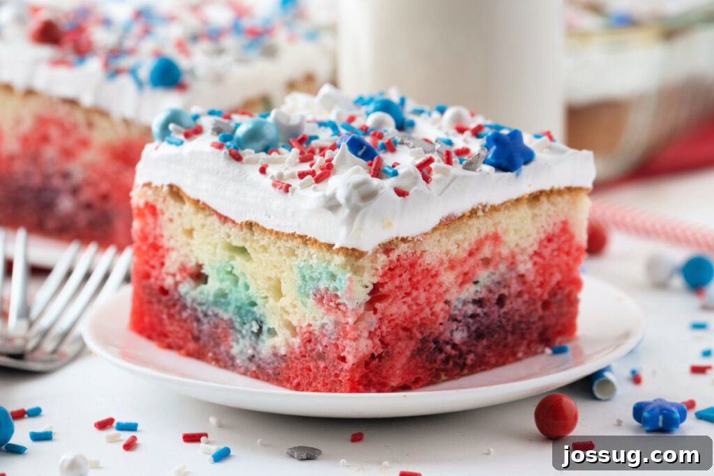 A beautifully presented slice of Patriotic Jello Poke Cake with visible red and blue jello layers, garnished with sprinkles on a plate