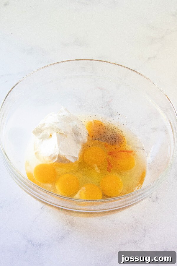 A bowl filled with a creamy mixture of beaten eggs, sour cream, salt, and red pepper sauce, ready for further ingredients.