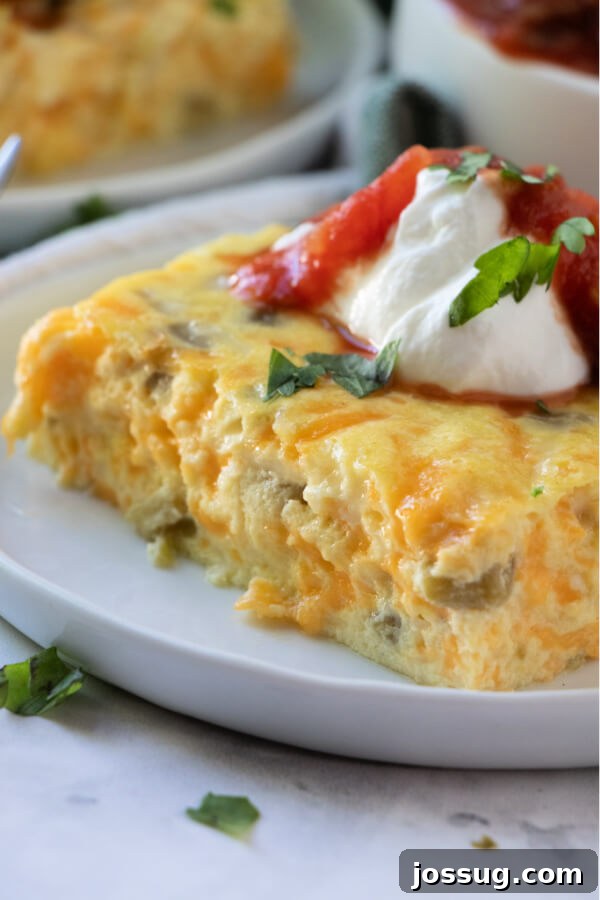A close-up shot of a perfectly baked and garnished slice of Chili Rellenos Bake, showing the melty cheese and tender egg base, topped with sour cream and salsa.