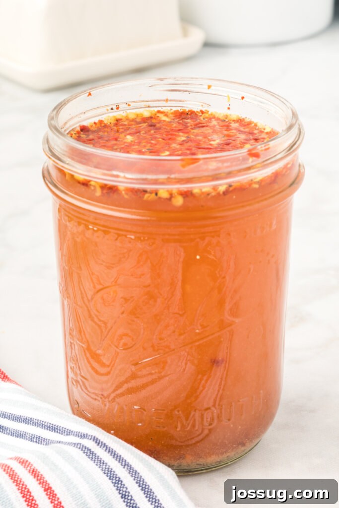 Glass jar filled with vibrant red Eastern NC vinegar-based BBQ sauce, showcasing its rich color and thin consistency