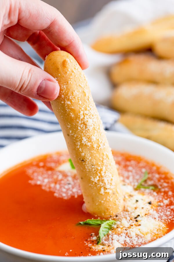 A hand dipping a Soft Italian Breadstick into a bowl of vibrant red marinara sauce.