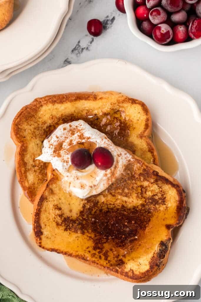 Eggnog Infused Brioche 2 Overhead view of Eggnog French Toast with whipped cream, cinnamon, and cranberries, surrounded by a bowl of fresh berries.