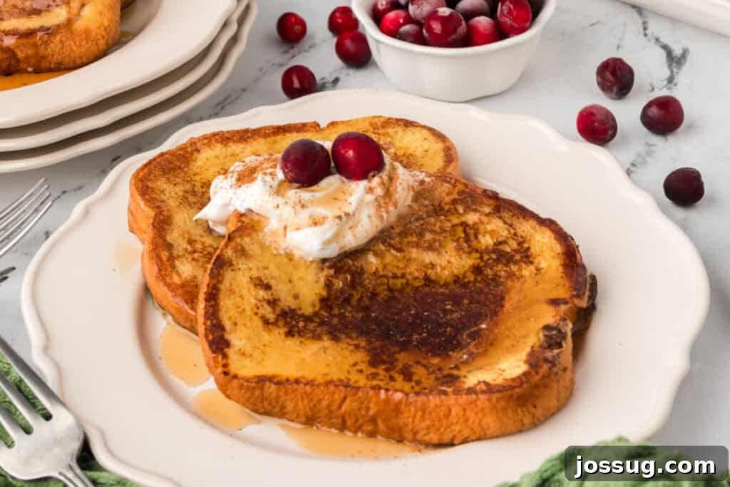 Eggnog Infused Brioche 10 Two slices of Eggnog French Toast on a white plate topped with whipped cream, syrup, and cranberries, styled for the holidays.
