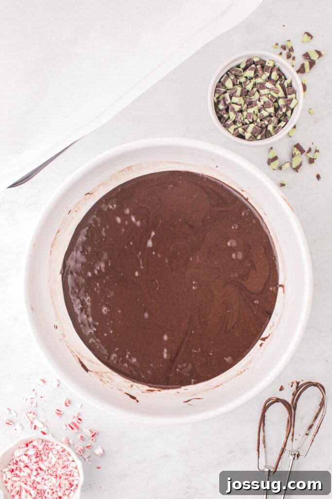 Candy Cane Swirl Brownies 4 A bowl of freshly mixed chocolate brownie batter with a smooth texture, with bowls of mint baking chips and crushed candy canes nearby.
