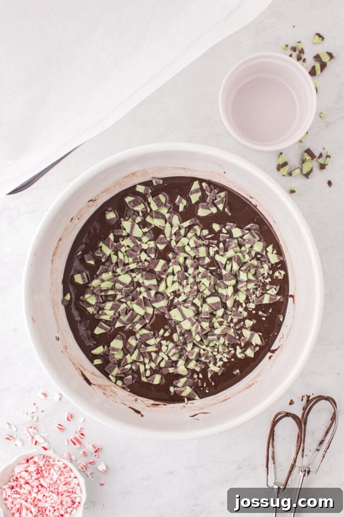 Candy Cane Swirl Brownies 5 Mint fudge baking chips scattered on top of unblended brownie batter in a large white mixing bowl.