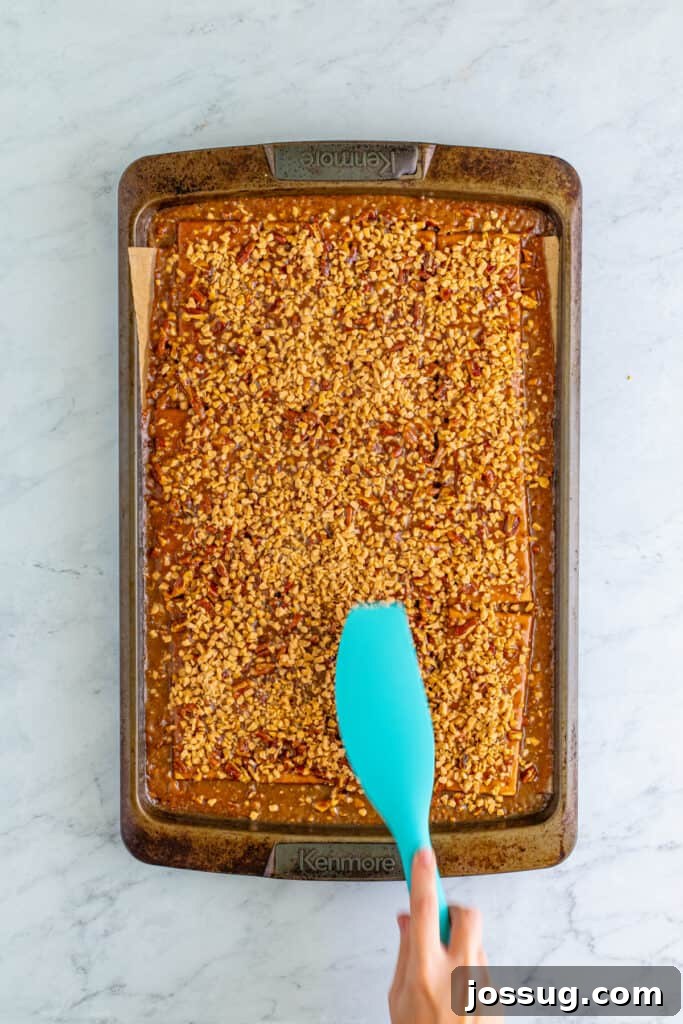 Toffee Graham Bliss Bites 9 Hand using a spatula to gently press toffee bits into the caramel layer on graham crackers