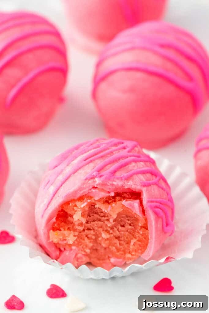 Pink Valentine truffles with a bite taken out, revealing a soft cake center and smooth pink coating.